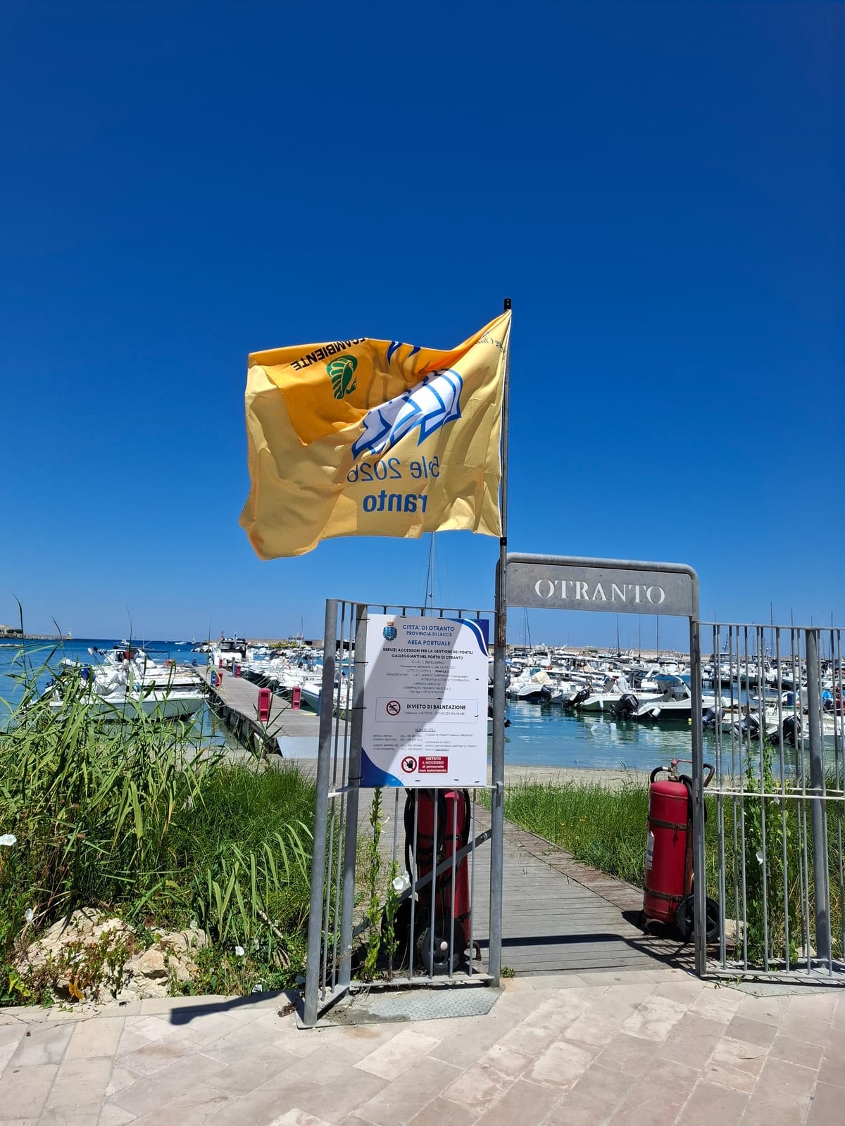 Pier entrance at the port of Otranto: gate with OTRANTO sign and yellow flag